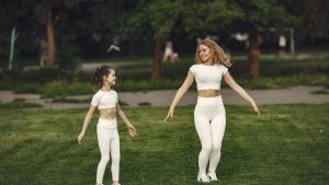 Mother and daughter bonding through outdoor exercise in activewear, featuring a joyful moment in a green park.